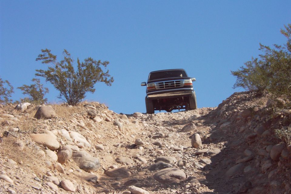 Dark lifted Ford Bronco cresting a rocky desert hill, front end against blue sky