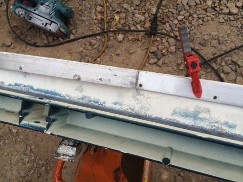 1995 Ford Bronco - A close-up view of a vehicle body panel, possibly undergoing restoration, with a belt sander and clamp visible in the background.