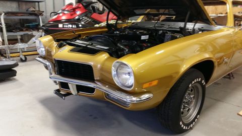 1970 Chevrolet Camaro - The front end of a gold 1970 Chevrolet Camaro is visible with its hood up, revealing the engine bay.