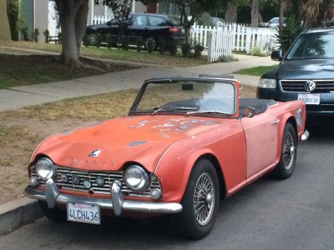 1968 Ford Mustang - This orange Triumph TR4 convertible is parked on a residential street next to a dark SUV.