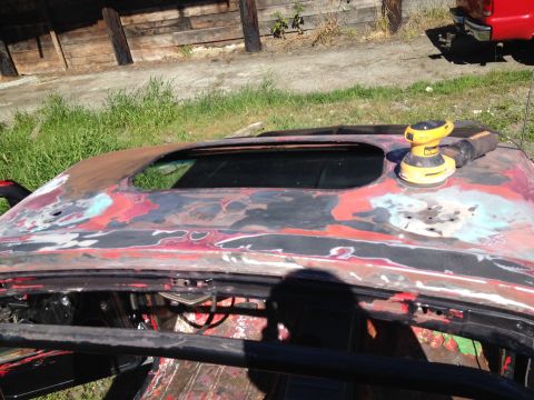 1978 Ford Bronco - A car roof is being sanded down to primer, with a power sander resting on it.