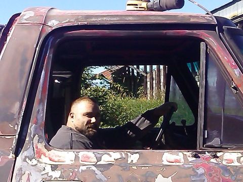 1978 Ford Bronco - A man is seated in the driver's seat of a heavily weathered truck, with a rural landscape visible through the windows.
