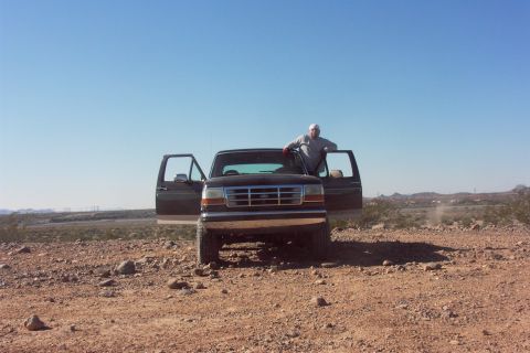 1992 Ford Bronco - Head-on view of a lifted dark brown Ford Bronco with both doors swung open, chrome bumper and Ford-badged grille, parked on open rocky dese…