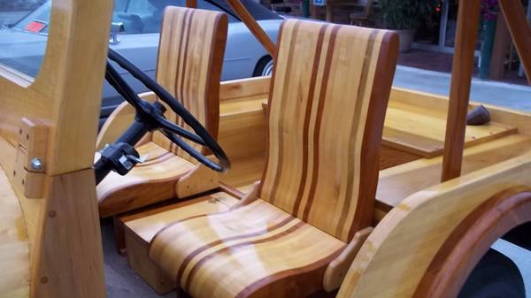 Wooden car interior with striped seats and steering wheel. A light-colored car is visible in the background