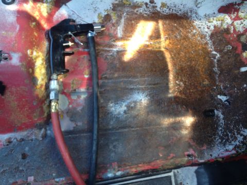 1978 Ford Bronco - Sandblaster gun connected to a hose, aimed at a heavily rusted metal surface.