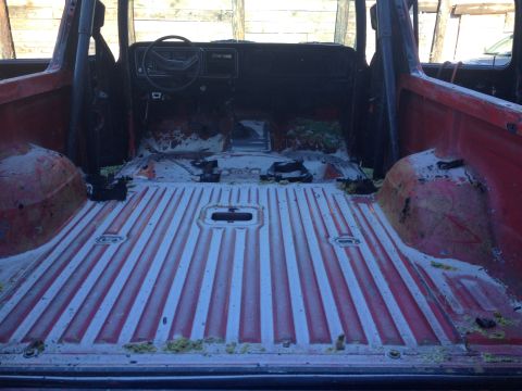 1978 Ford Bronco - The interior of a red SUV shows a stripped-down cabin with exposed metal flooring and dashboard.