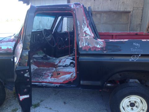 1978 Ford Bronco - This 1978 Ford pickup truck's interior is visible with the driver's side door ajar, revealing worn seats and dashboard details.