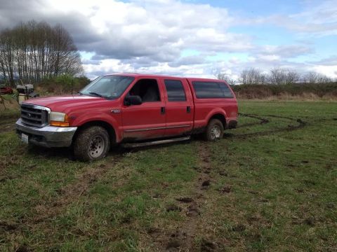 1999 Ford F-350 - A red Ford F-350 pickup truck is stuck in a muddy field with tire tracks showing it spun out.