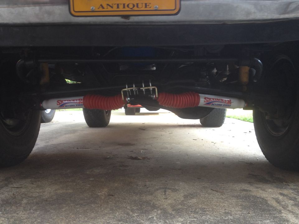 Underside of a vehicle showing a steering stabilizer with red bellows and yellow shocks