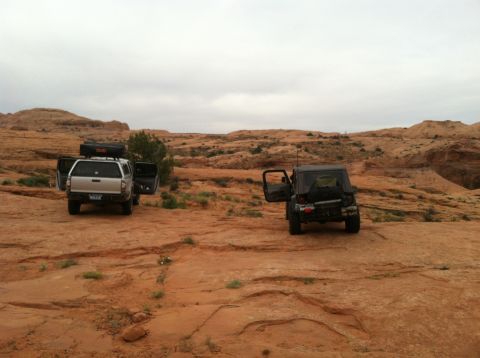 2005 Jeep Wrangler - Two off-road vehicles are parked on a rocky desert trail under an overcast sky.