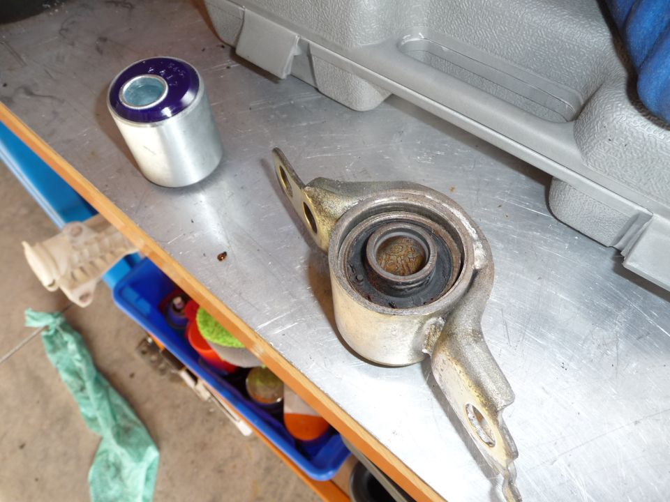 Car suspension control arm with old bushing and new blue bushing next to it