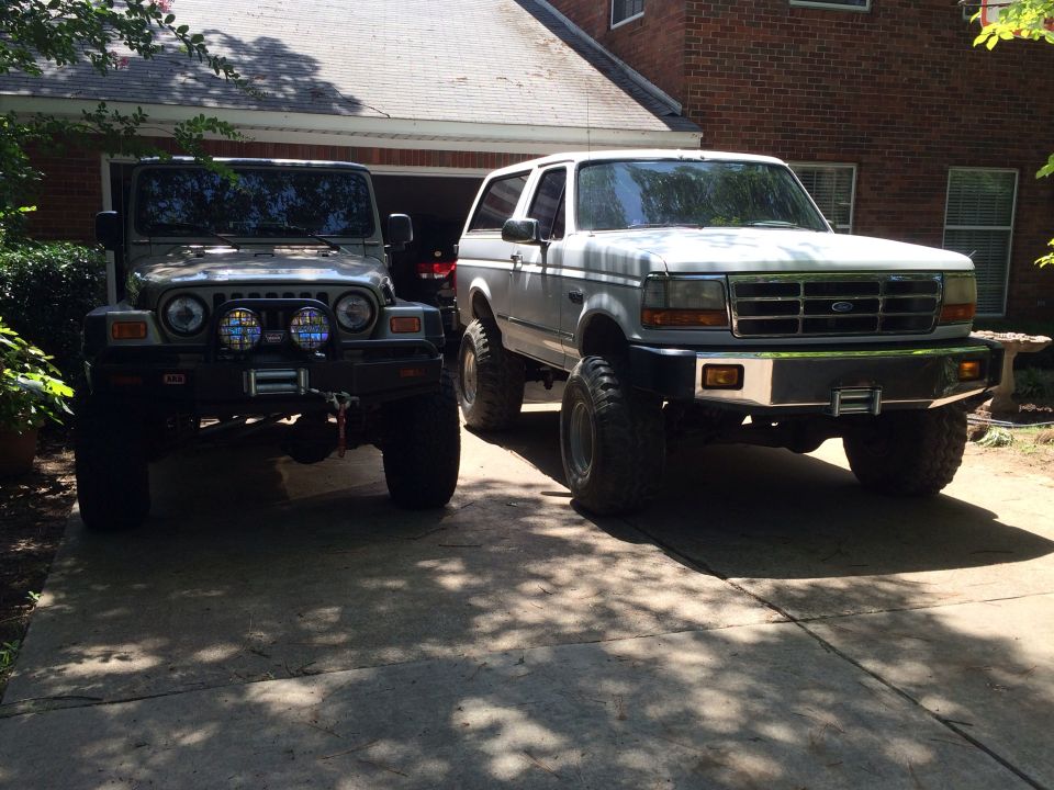 Jeep Wrangler and a lifted 1992 Ford Bronco parked in a driveway