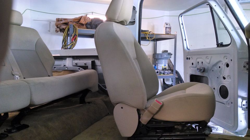 Vehicle interior showing removed seats and door panel, with shelves in background