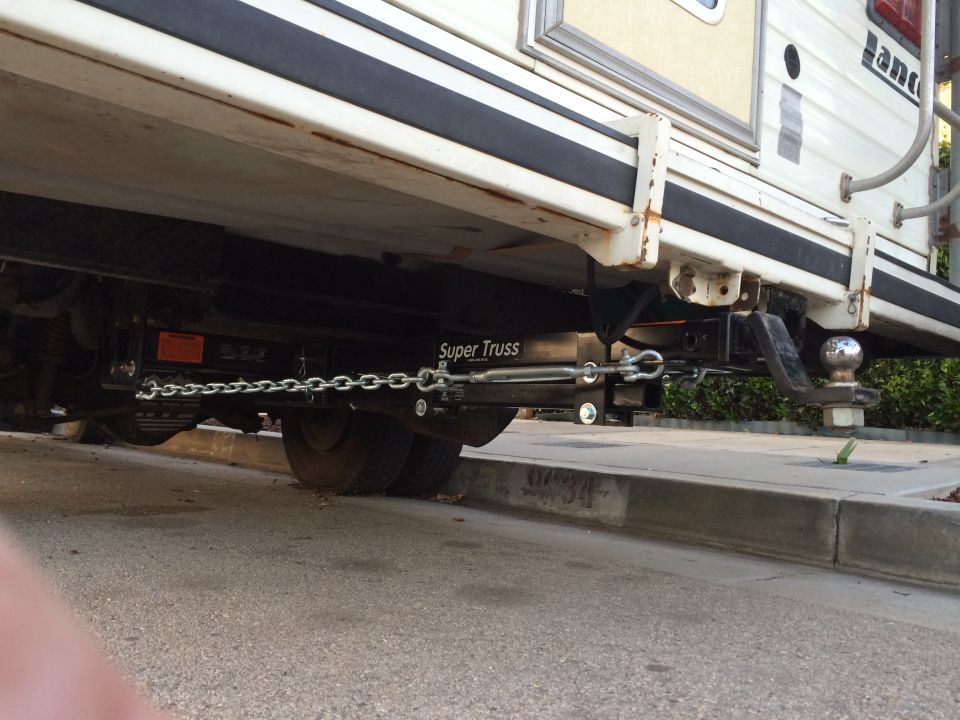 Trailer hitch extension with chains and ball mount attached to the underside of a camper