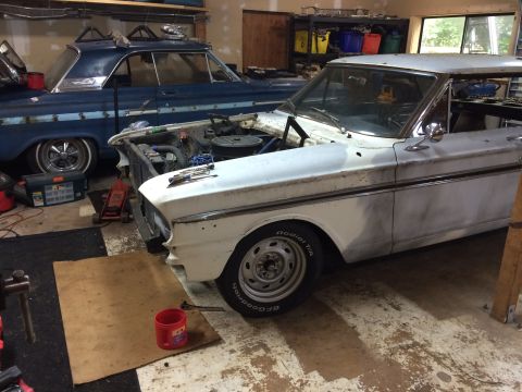 1964 Ford Fairlane - Two cars are in a garage, one white and one blue, with the white car's hood open and tools nearby.