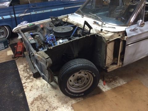 1964 Ford Fairlane - A white 1964 Ford Fairlane is partially disassembled in a garage, revealing its engine and front wheel assembly.