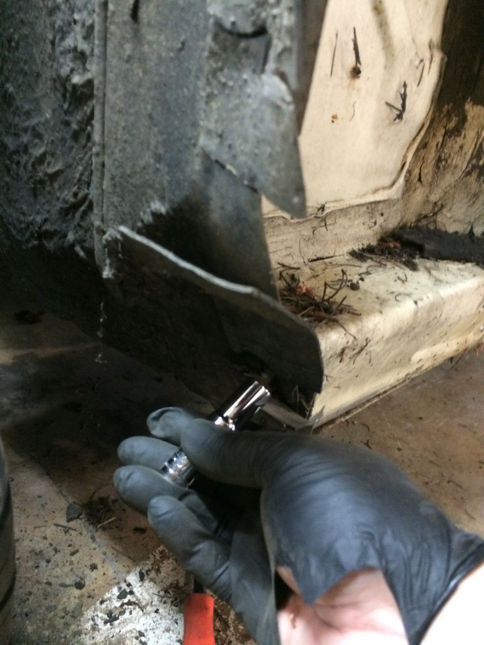Gloved hand holding a socket wrench near a rusty car frame section