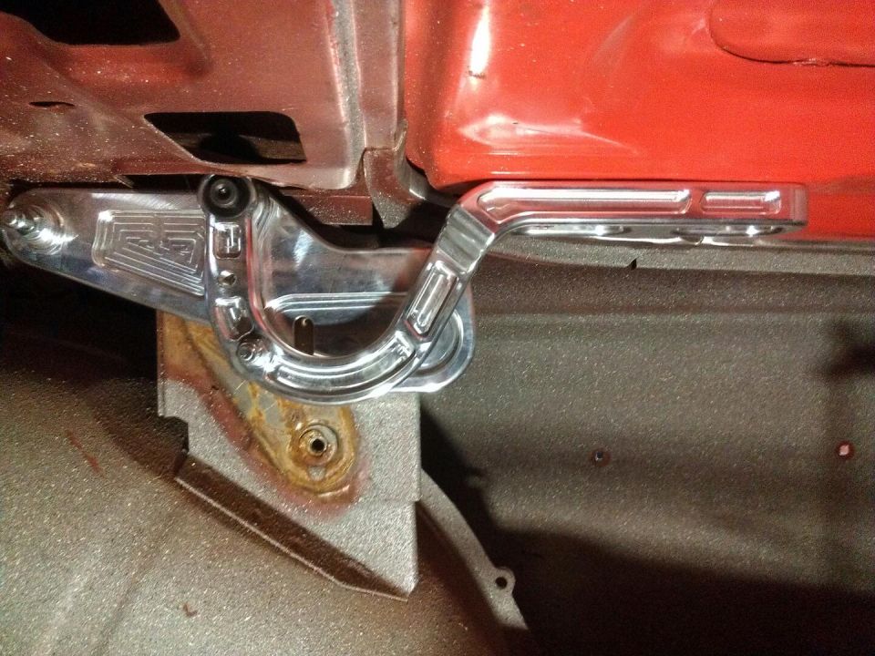 Polished aluminum custom hood hinge with engraved 'RS' logo, attached to red painted metal and rusty bracket