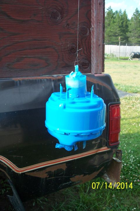 1978 Ford Bronco - A blue brake booster is suspended by a wire, likely for painting, with a portion of a truck visible in the background.