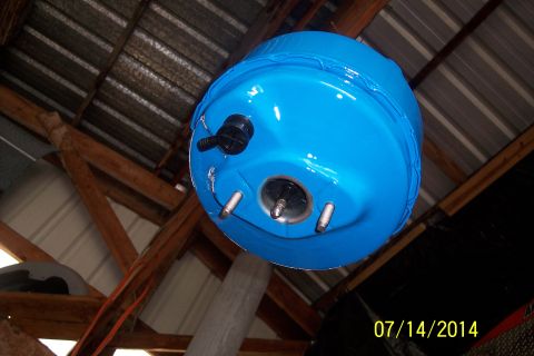 1978 Ford Bronco - A blue brake booster is pictured, likely for a vehicle, suspended from a workshop ceiling.