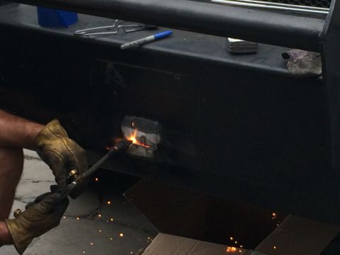 1997 Dodge 3500 - A person welds a metal component onto a black bumper, with sparks flying.