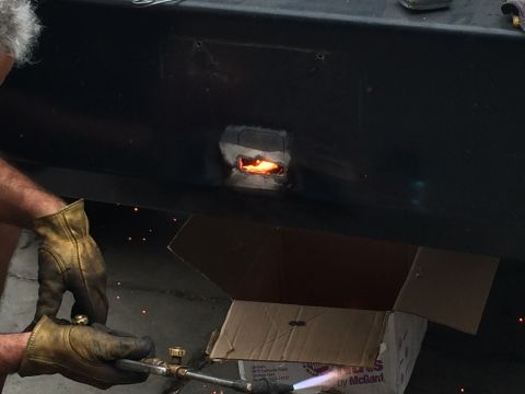 1997 Dodge 3500 - A person is welding a hole in a black metal surface, with sparks flying and a cardboard box in the background.