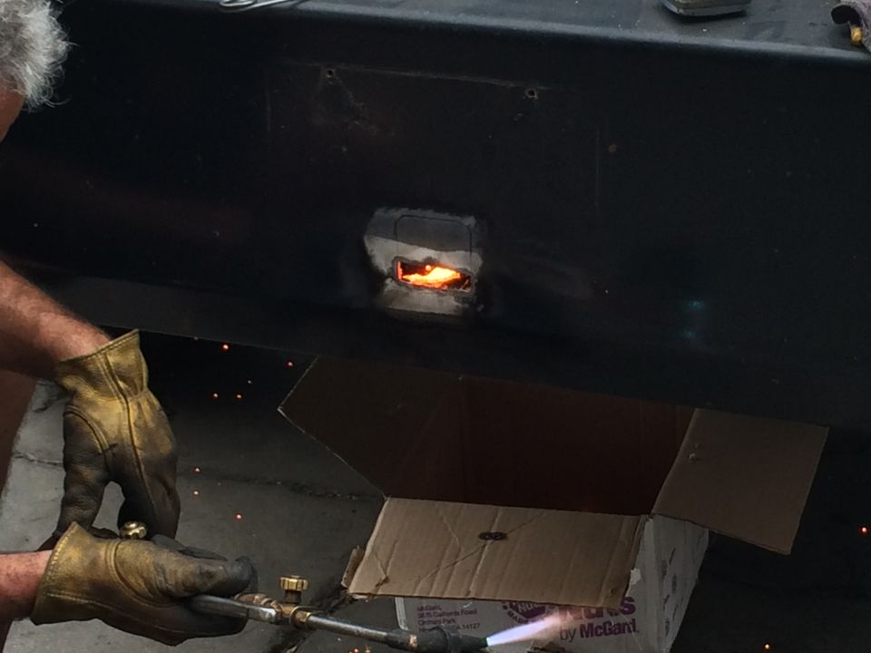 person welding a hole in black metal, sparks flying, cardboard box nearby