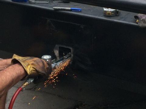 1997 Dodge 3500 - A person in a work glove uses a grinder on a black vehicle part, creating a shower of sparks.