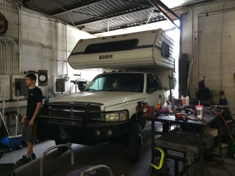 1997 Dodge 3500 - A white Dodge pickup truck is parked inside a garage, fitted with a Lance camper shell on its bed.