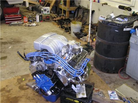 1993 Ford Bronco - Engine assembly with prominent blue spark plug wires and chrome exhaust headers sits on the floor of a workshop.
