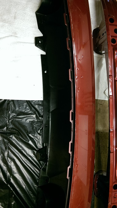 2015 Subaru Forester - Close-up of a red car bumper part with black plastic trim, showing water droplets and a website watermark.
