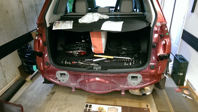 Rear of a red Subaru Forester with bumper removed, tools laid out in cargo area