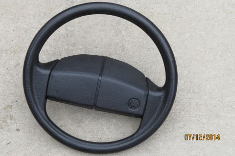 1985 Volkswagen Jetta - A black steering wheel with a Volkswagen logo is shown against a concrete background.