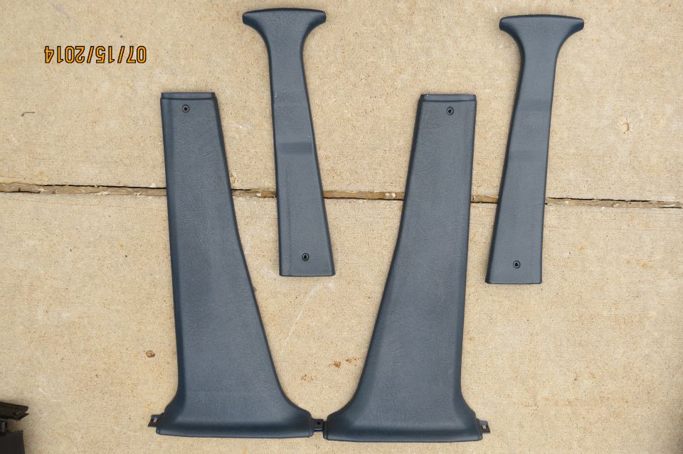 Four dark gray plastic interior trim pieces laid out on a concrete surface