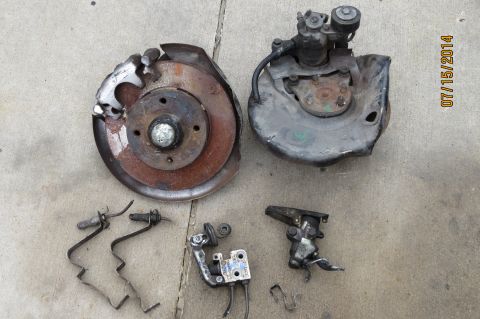 1985 Volkswagen Jetta - Various brake system components, including a rotor, caliper, and hub, are displayed on a concrete surface.