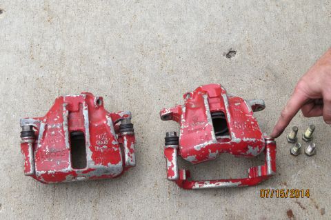 1985 Volkswagen Jetta - Two red brake calipers are shown on a concrete surface, with a hand indicating a detail on one of them.