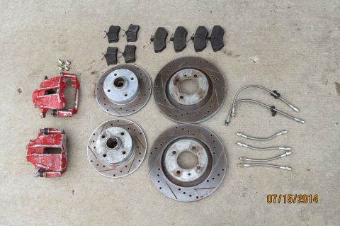 1985 Volkswagen Jetta - A collection of red brake calipers, drilled rotors, and brake pads are displayed on a concrete surface, along with braided steel brake line…