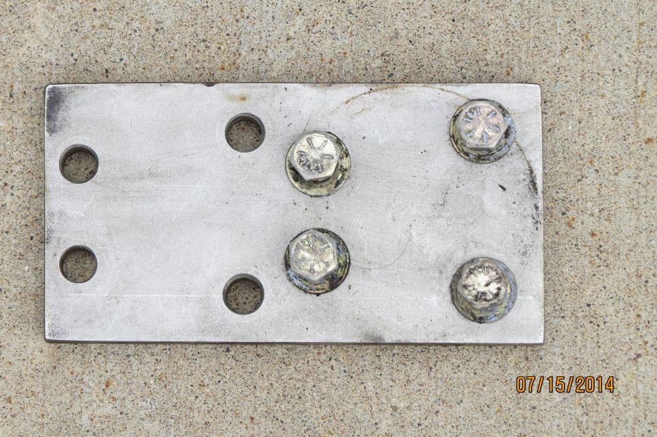 Metal plate with six bolt holes and five bolts attached, resting on concrete