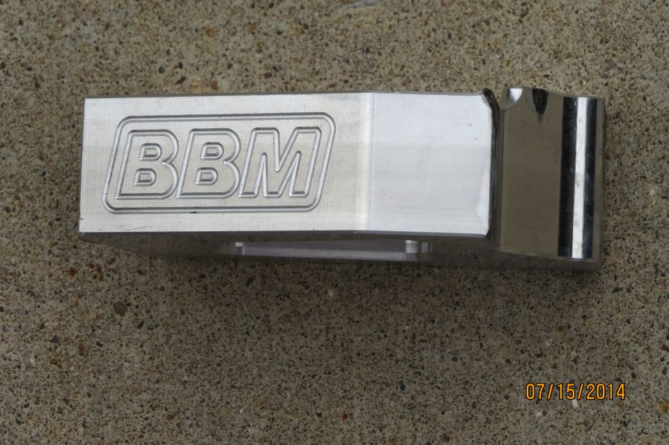 Metal part with engraved 'BBM' logo, resting on concrete