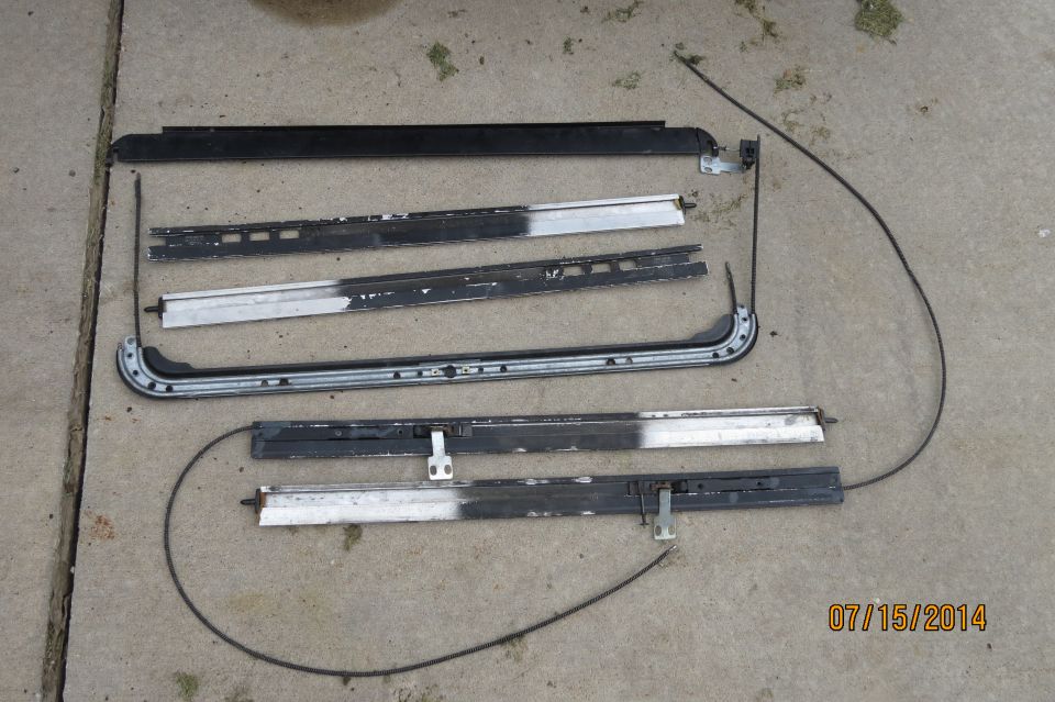 Disassembled sunroof components including tracks and cables laid out on concrete