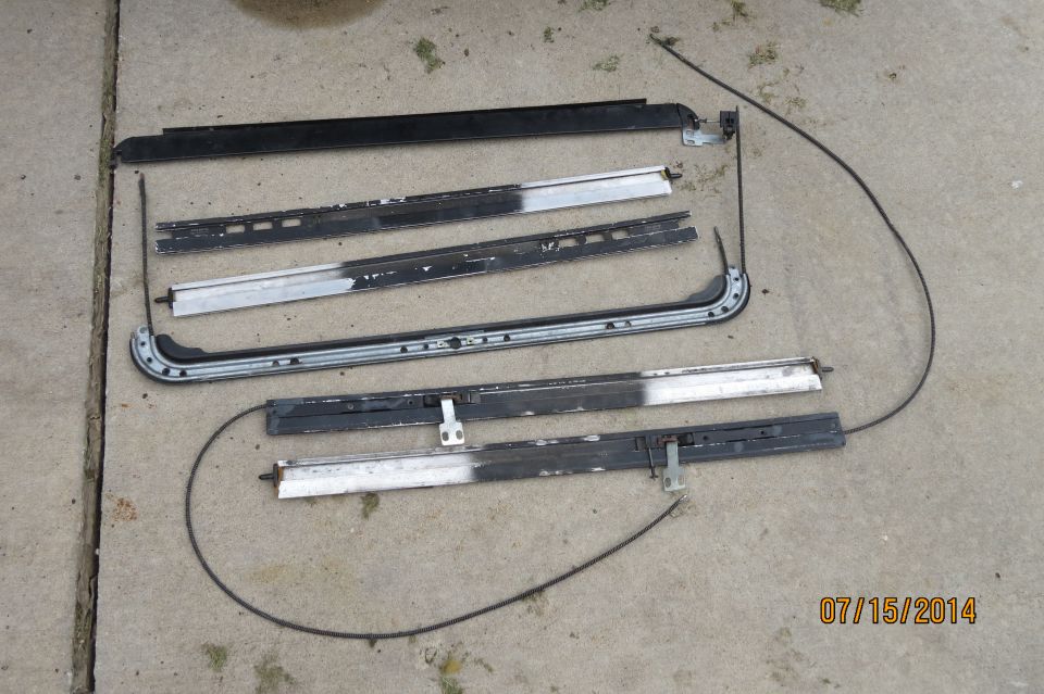 Disassembled sunroof tracks and cables laid out on concrete