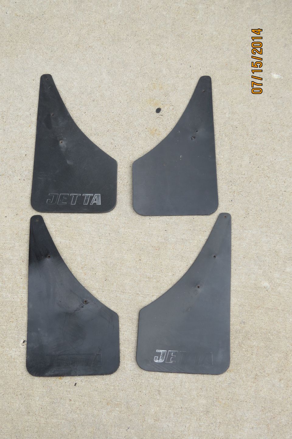 Four black mud flaps with "JETTA" embossed on two of them, laid out on a concrete surface