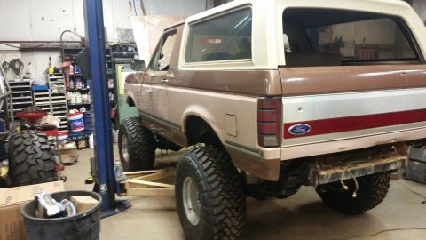 1988 Ford Bronco - This lifted 1988 Ford Bronco is seen in a garage with its hood up and large off-road tires.