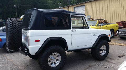 1988 Ford Bronco - A white Ford Bronco with a black soft top is parked next to other vehicles outside a building.