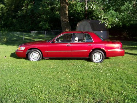 1999 Mercury Grand Marquis - A red 1999 Mercury Grand Marquis sedan is parked on a grassy lawn next to a tree and shed.