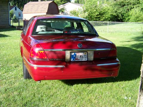 1999 Mercury Grand Marquis - Rear view of a red Mercury Grand Marquis sedan parked on a grassy lawn with a fence and houses in the background.