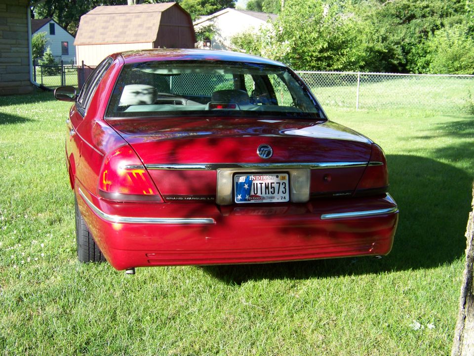 Red Mercury Grand Marquis sedan parked on grass, rear view. License plate reads UTH573