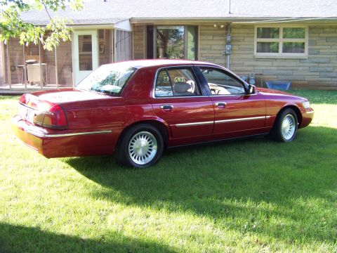 1999 Mercury Grand Marquis - Red sedan parked on grass in front of a house. The car is likely a Mercury Grand Marquis, but the year is not 1999.