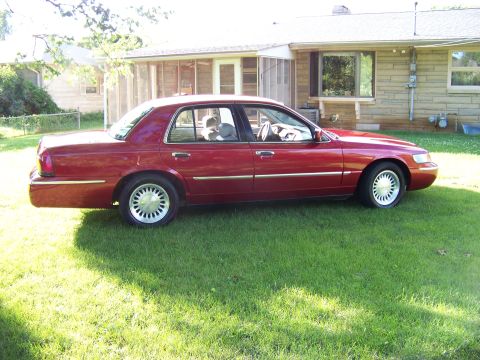 1999 Mercury Grand Marquis - This red 1999 Mercury Grand Marquis is parked on the grass in front of a house.