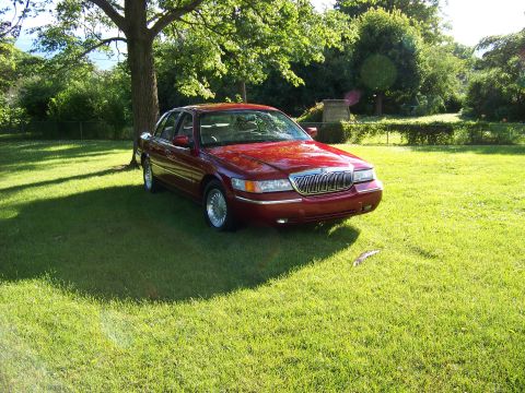 1999 Mercury Grand Marquis - A red 1999 Mercury Grand Marquis is parked on a grassy lawn under a large tree.